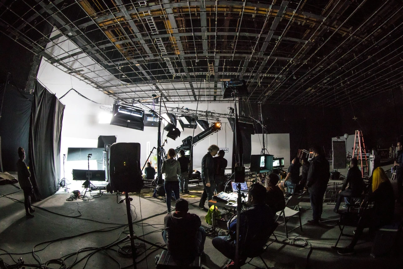 A film crew working on a large soundstage with lighting equipment and cameras